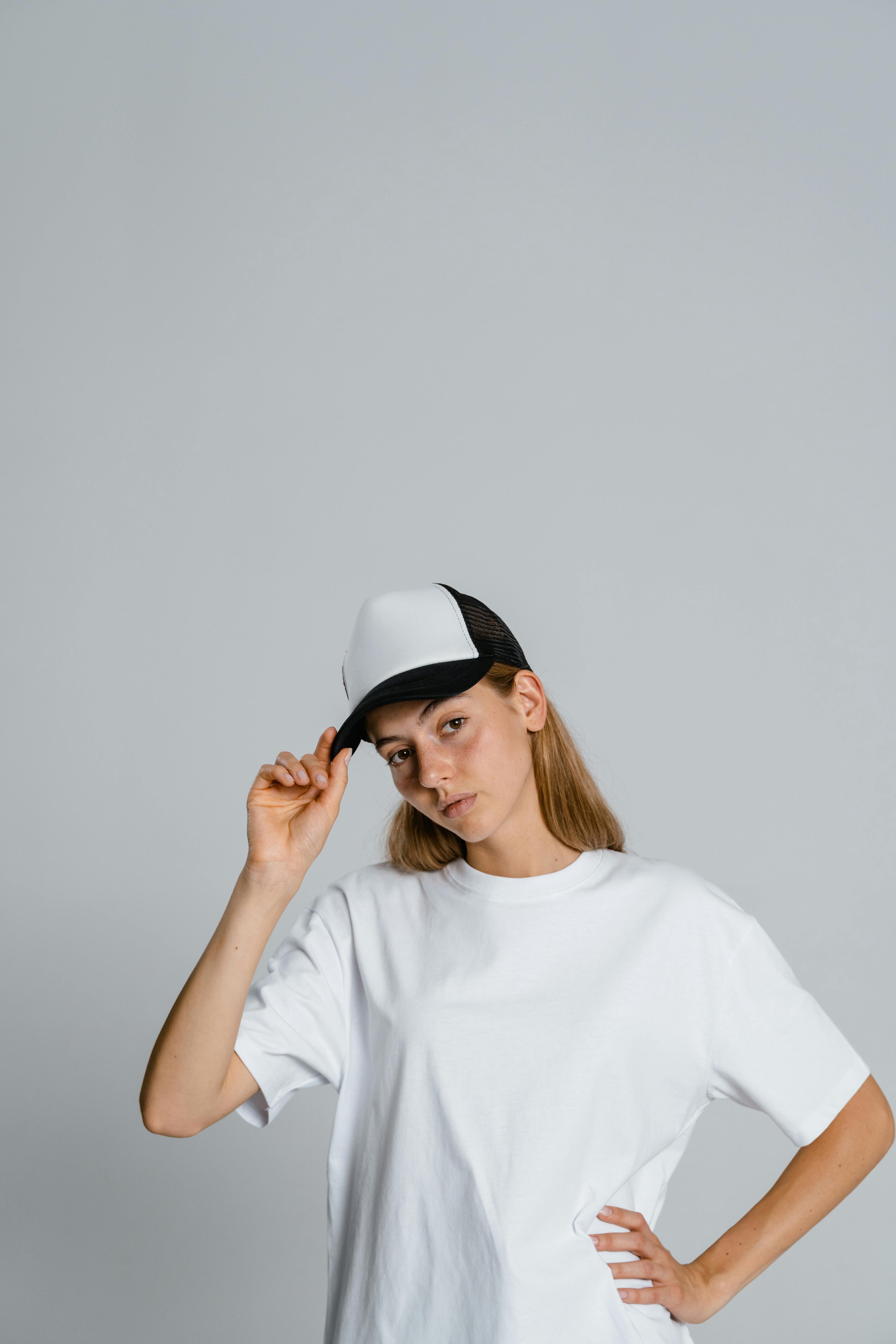 Person wearing a white and black cap and white t-shirt on a gray background